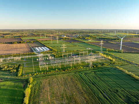 Electrical substation with large-scale battery energy storage system (BESS) installation, power lines, and wind turbines in the background.