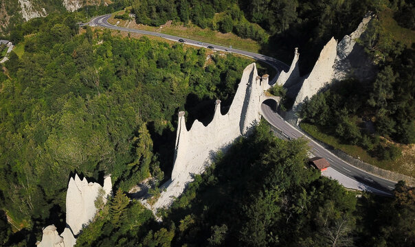 Aerial view of Pyramides d'Euseigne earth pyramids with a road tunnel passing through the rock formations surrounded by dense green forest Heremence, Valais, Switzerland.