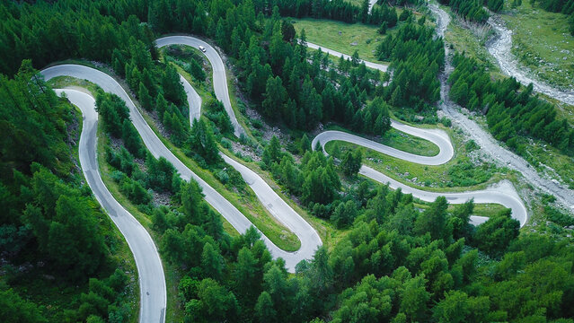 Aerial view of a winding serpentine road with hairpin turns through a dense green coniferous forest Heremence, Valais, Switzerland.