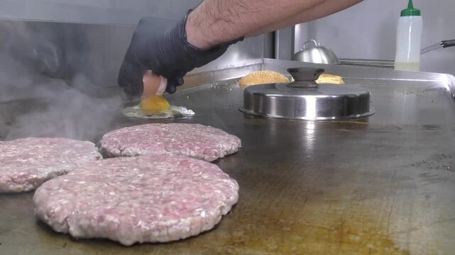 Preparazione di un panino hamburger su piastra. Panino hamburger grigliato con pancetta, cipolla glassata, formaggio e uova