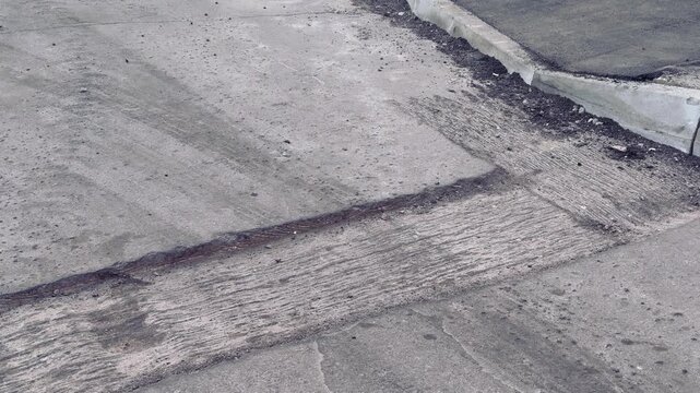 Damaged asphalt curb corner with aggregate, scattered loose asphalt and gravel along cracked pavement next to grassy verge