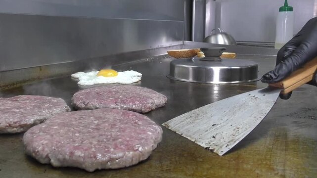 Preparazione di un panino hamburger su piastra. Panino hamburger grigliato con pancetta, cipolla glassata, formaggio e uova