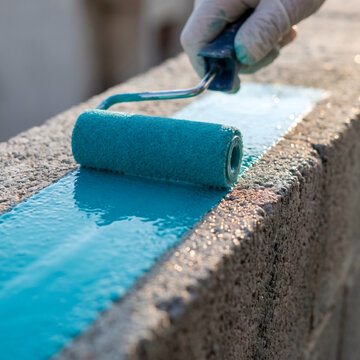 Worker applying blue waterproof coating on concrete surface with paint roller