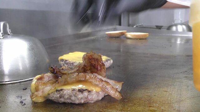 Preparazione di un panino hamburger su piastra. Panino hamburger grigliato con pancetta, cipolla glassata, formaggio e uova