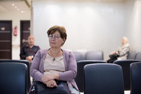 Elderly woman waiting in a Middle Eastern eye hospital clinic waiting room with distant patients
