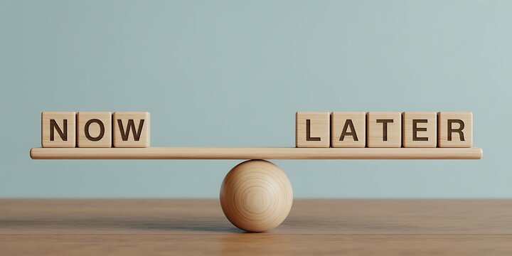 A wooden seesaw with blocks spelling now and later in balance on a table
