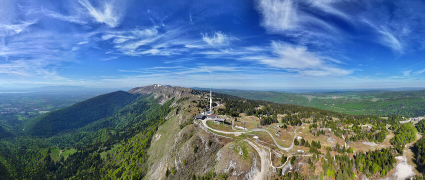 Aerial view of Col de la Faucille mountain pass with its telecommunications tower, winding roads, and lush green slopes under a blue sky Gex, Auvergne-Rhone-Alpes, France.