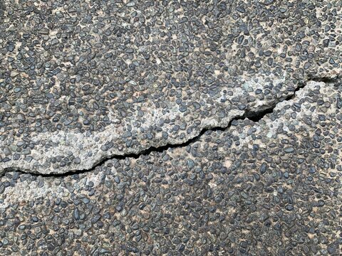 Weathered pebble concrete pavement showing a long structural crack and exposed aggregate texture