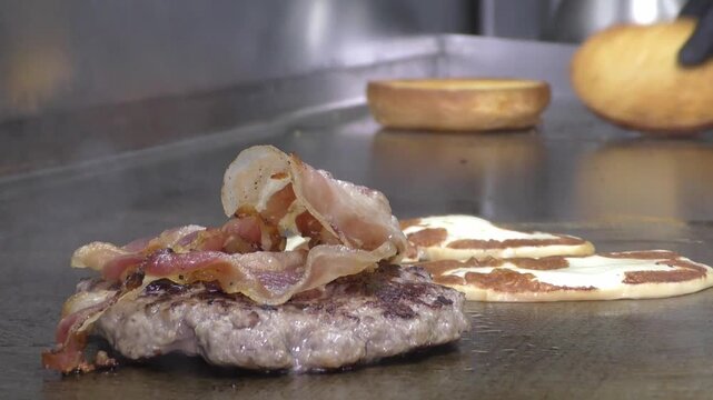 Preparazione di un panino hamburger su piastra. Panino hamburger grigliato con pancetta, cipolla glassata, formaggio e uova