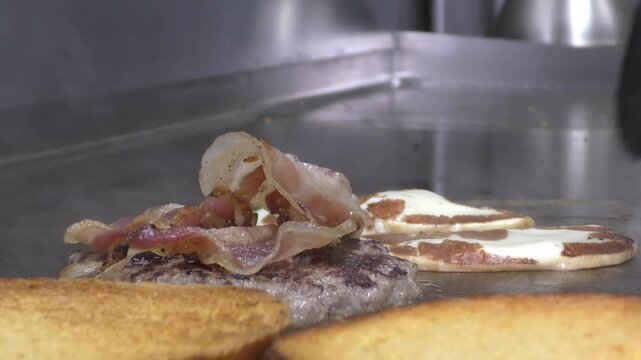 Preparazione di un panino hamburger su piastra. Panino hamburger grigliato con pancetta, cipolla glassata, formaggio e uova