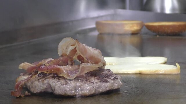 Preparazione di un panino hamburger su piastra. Panino hamburger grigliato con pancetta, cipolla glassata, formaggio e uova