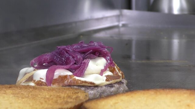 Preparazione di un panino hamburger su piastra. Panino hamburger grigliato con pancetta, cipolla glassata, formaggio e uova