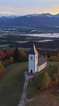 Stunning aerial view of the iconic Church of Saints Primus and Felician in Jamnik, Slovenia, surrounded by autumn colors at sunrise