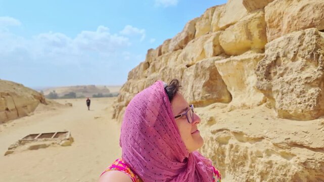 Happy female tourist wearing a headscarf  or hijab taking a video selfie while visiting the giza pyramids in the egyptian desert on a sunny day