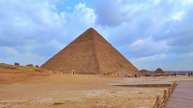 Historical great pyramid of giza under a cloudy sky. Majestic ancient egyptian monument in the desert with people walking on the sand
