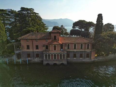 Aerial view of a historic lakeside villa with arched windows and terracotta roof tiles on the shore of Lake Iseo in Monte Isola, Lombardy, Italy.