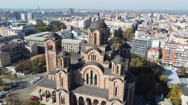 Descending drone video shows Saint Mark Church from its domes to the ground level, highlighting the architecture on a sunny day, Belgrade, Serbia.