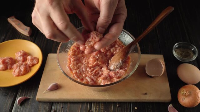 Hands mixing ground meat and eggs in a glass bowl, surrounded by garlic, onion, and eggs on a wooden table in a cozy kitchen setting