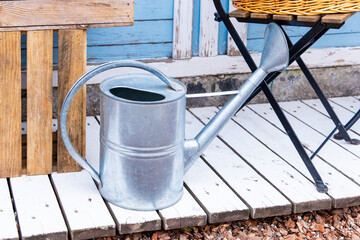 Naklejka premium Garden scene with a rustic watering can beside a wooden bench and a wicker basket under a charming blue backdrop