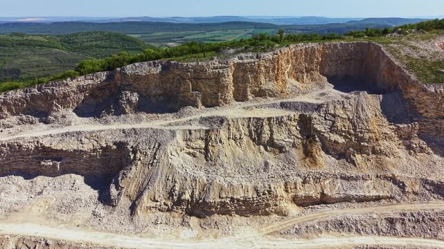 A limestone quarry is visible with layers of rock and earth. Machinery is present, and workers are seen moving materials. The landscape includes rolling hills under sunny skies.