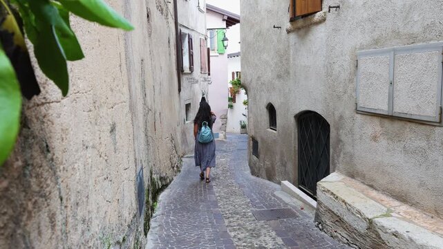 LIMONE SUL GARDA, ITALY - MAY 20, 2025: A female traveler with a blue backpack exploring the narrow stone streets of the old town in Limone.