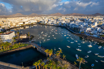 Fototapeta premium Discover the coastal view of Arrecife in Lanzarote. This location features buildings along the waterfront, palm trees, and distant mountains. Enjoy the vibrant atmosphere and unique architecture.