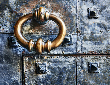 Antique drop ring handle or ring door knocker against an old metal door, Genoa, Italy, Europe 