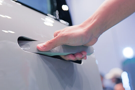 A person opening a modern, flush-mounted retractable door handle on a glossy vehicle. Design makes it sleek looking but has questionable emergency uses.