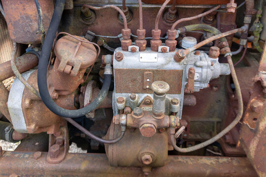 Close view of an old diesel engine fuel injection pump with rusted pipes, bolts, hoses, and metal fittings. The image shows vintage machinery, mechanical repair, industrial texture, corrosion, and hea