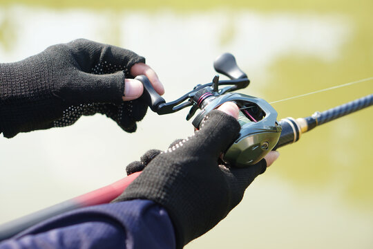 Close-up of angler hands using a baitcasting reel and fishing rod outdoors on a sunny day. Sport fishing activity with selective focus, outdoor recreation and hobby concept.