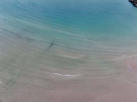 Aerial view of Gruinard Bay featuring turquoise water, gentle waves, and sand ripples on the shore in Gruinard, Scotland, United Kingdom.