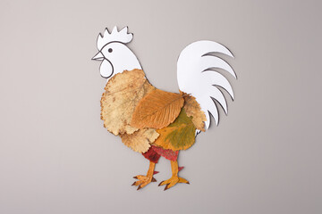 Handmade rooster collage using dried autumn leaves and white paper cutout on grey background. Creative DIY concept for organic farms, eco-friendly brands, and educational craft workshops © Elena