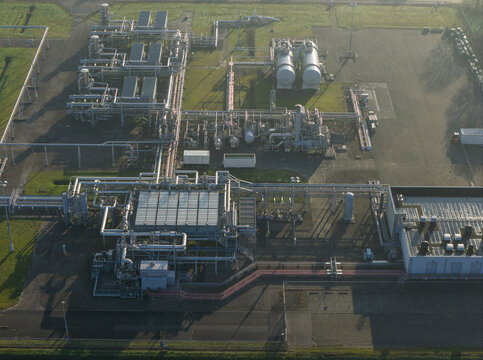 Aerial view of the natural gas mining facility with complex pipelines, storage tanks, and industrial infrastructure under soft morning light Slochteren, Groningen, Netherlands.
