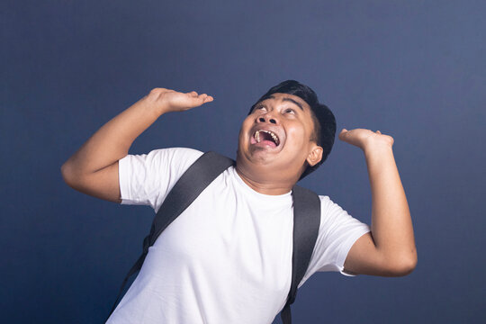 Young student with a backpack looks up with a scared and fearful expression at something above him.