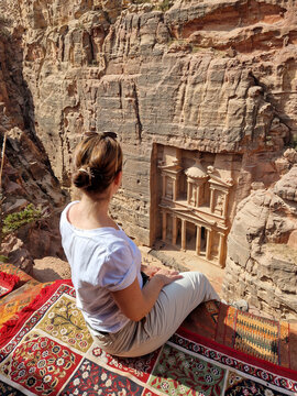 Eine junge Frau sitzt auf einem bunten Teppich und blickt auf die antike Felsenstadt Petra Khazne al-Firaun in Jordanien, eines der Sehensw&uuml;rdigkeit auf jeder Reise