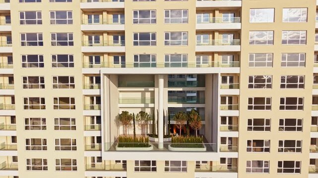 A large residential building features a unique open balcony with greenery well placed between two sections. Sunlight reflects on the glass windows of the structure.