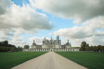 Obraz premium Visitors wander leisurely along the tree-lined path leading to the majestic Château de Chambord, embracing the tranquil charm of this historic landmark under soft, diffused light