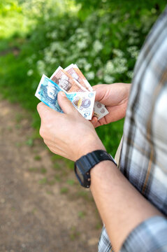 Man holding British pound banknotes outdoors near green foliage, personal finance, budgeting concept, cash payment, everyday economy.