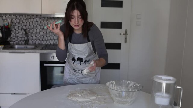 Young woman asks for help while sticky dough fails in her home kitchen creating messy baking stress with phone recipe flour covered hands and homemade cooking frustration