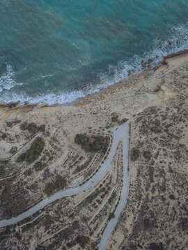 Aerial view of Santuari iber i roma de la Malladeta on a rocky cliff overlooking the turquoise Mediterranean Sea with winding paths and coastal vegetation La Vila Joiosa, Comunidad Valenciana, Spain.