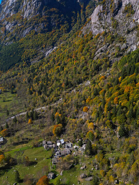 Aerial view of Val di Mello with autumn forest colors on steep rocky slopes and a small stone village in Val Masino, Lombardia, Italy.