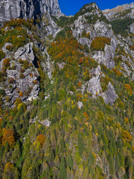 Aerial view of the Val di Mello granite cliffs and dense forest with vibrant autumn foliage under a clear blue sky in Val Masino, Lombardia, Italy.