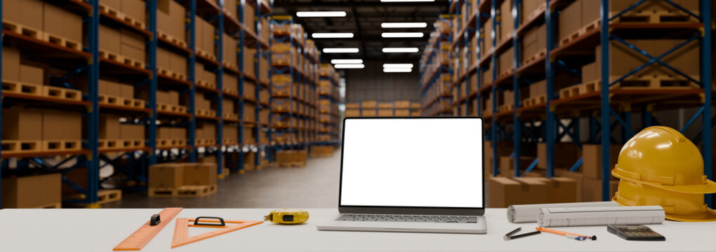 Engineering workspace empty screen laptop computer with safety equipment and drafting tools inside modern warehouse