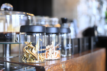 Obraz premium Dried Mushrooms in Glass Jars with Black Lids Displayed on Wooden Bar Counter at Specialty Cafe