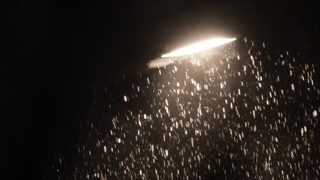 Snowfall against the background of light from a street lamp at night