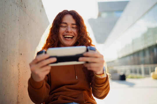 Excited laughing ginger man playing online game with mobile phone controller outside, success achievement, joy emotion, digital entertainment, lifestyle, tech user, mobile application, gaming device.