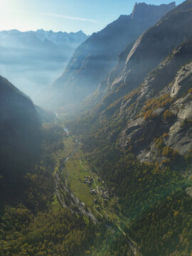 Aerial view of the Val di Mello valley with its steep granite cliffs, winding river, and autumn forests under a light morning mist in Val Masino, Lombardia, Italy.