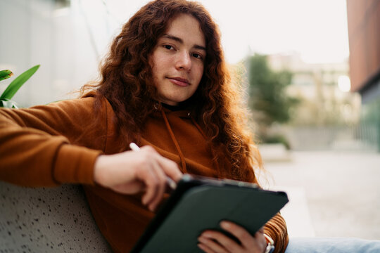 Caucasian redhead man sitting outdoors using digital tablet with stylus looking at camera, creative professional working on project, digital nomadic lifestyle, online education, 5G connection.