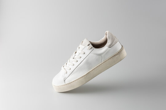 Trendy fashionable grey white leather in dirty grunge style women pair sneakers flying on neutral background. Casual style. Summer and spring shoes collection.