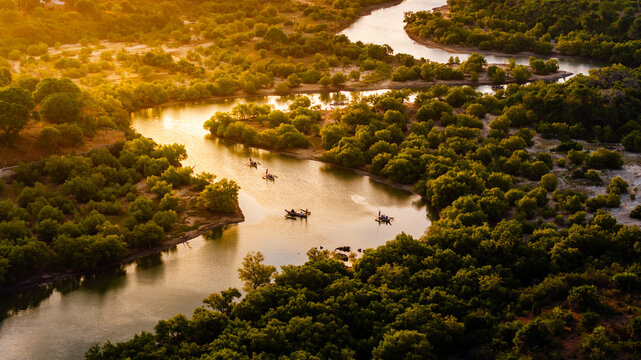 Aerial view of Congo River Diani winding through lush green mangroves with traditional boats and people during golden hour Diani Beach, Kwale County, Kenya.